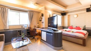 Een compacte hotelkamer met een bed, een bureau met een televisie, een kleine kitchenette en een zithoek met een tafel en stoelen.