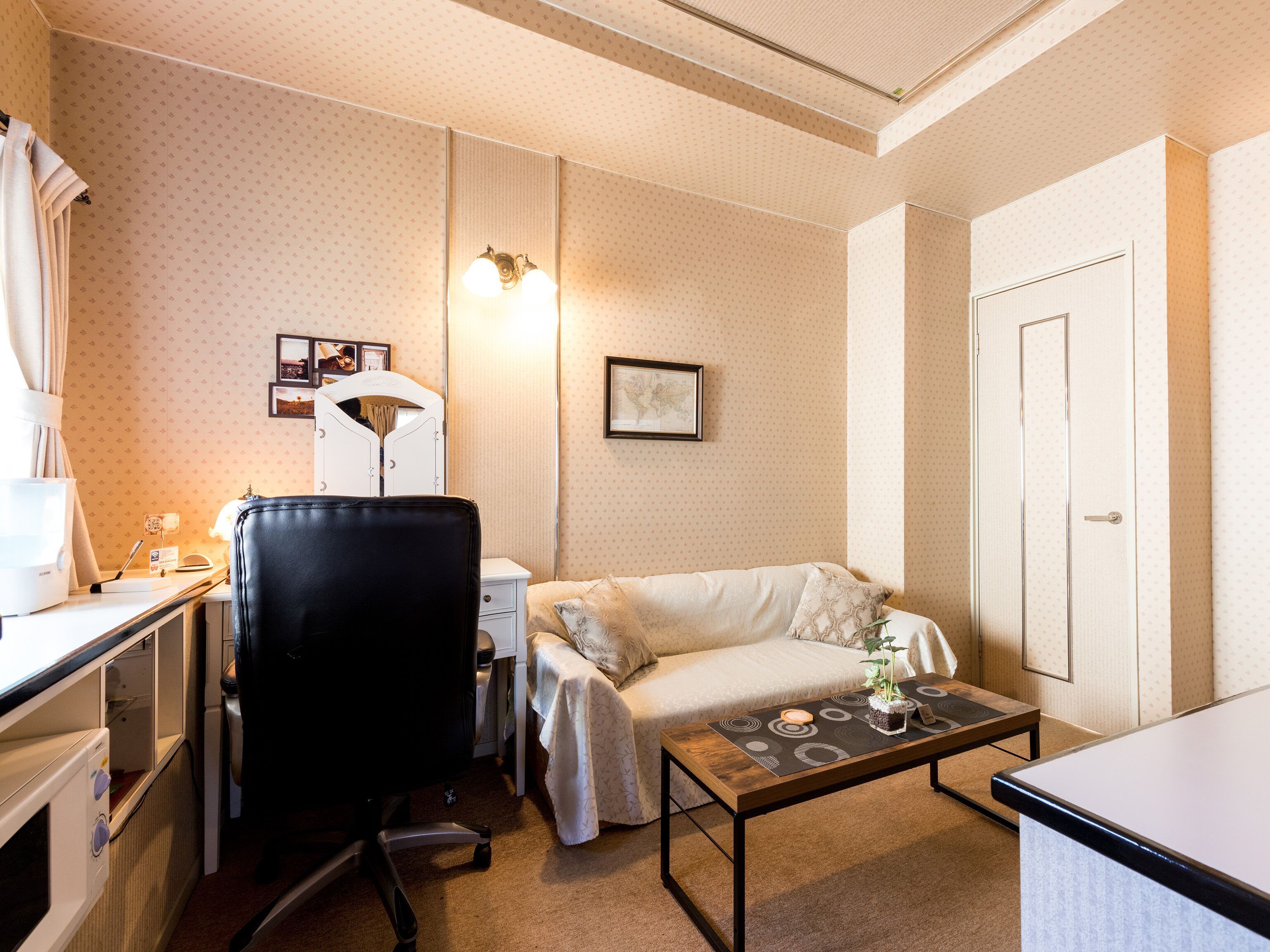 Una habitación de hotel con cama, escritorio con lámpara, silla, mesita con planta y puerta.