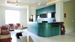 A reception area with a teal reception desk, a chandelier, a fire extinguisher, and a sofa with a red and white patterned throw. - Hotel Shivalik - Best Himalaya View Hotel In Almora' (Almora)