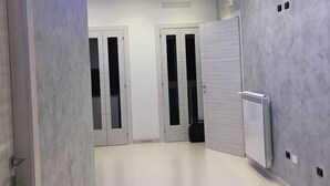 Un pasillo con pisos de baldosas blancas, paredes grises y una tira de luz LED azul. Hay puertas blancas con manijas negras y un radiador en la pared.