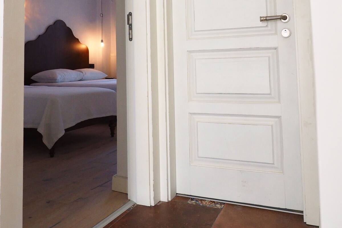Une chambre d’hôtel avec un lit, une table de chevet et une porte portant un numéro.