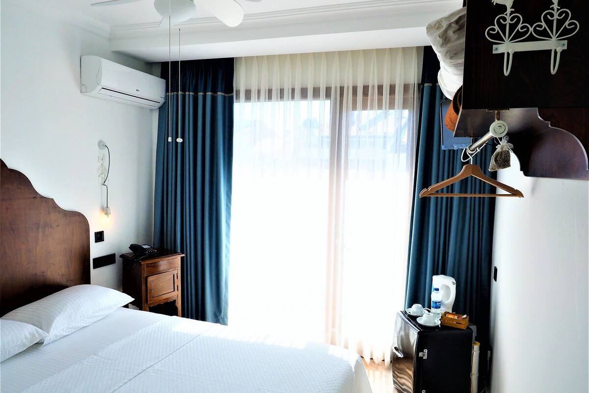 Une chambre d’hôtel avec un lit, un bureau avec une lampe, une armoire et une fenêtre avec des rideaux.