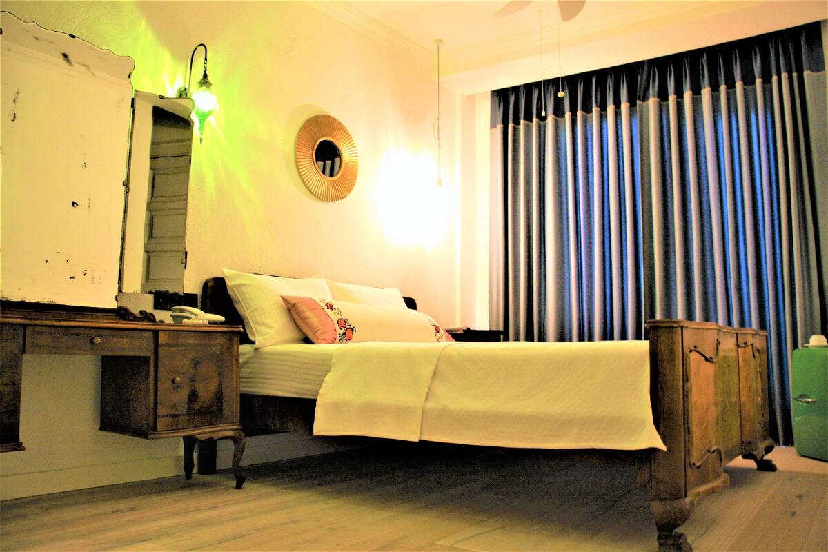 Une chambre à coucher avec un lit, une commode, un miroir et une fenêtre avec des rideaux.