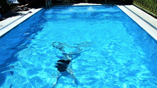 A swimming pool with clear blue water and a swimmer in the center. - Foca 1887 Otel (Foça)