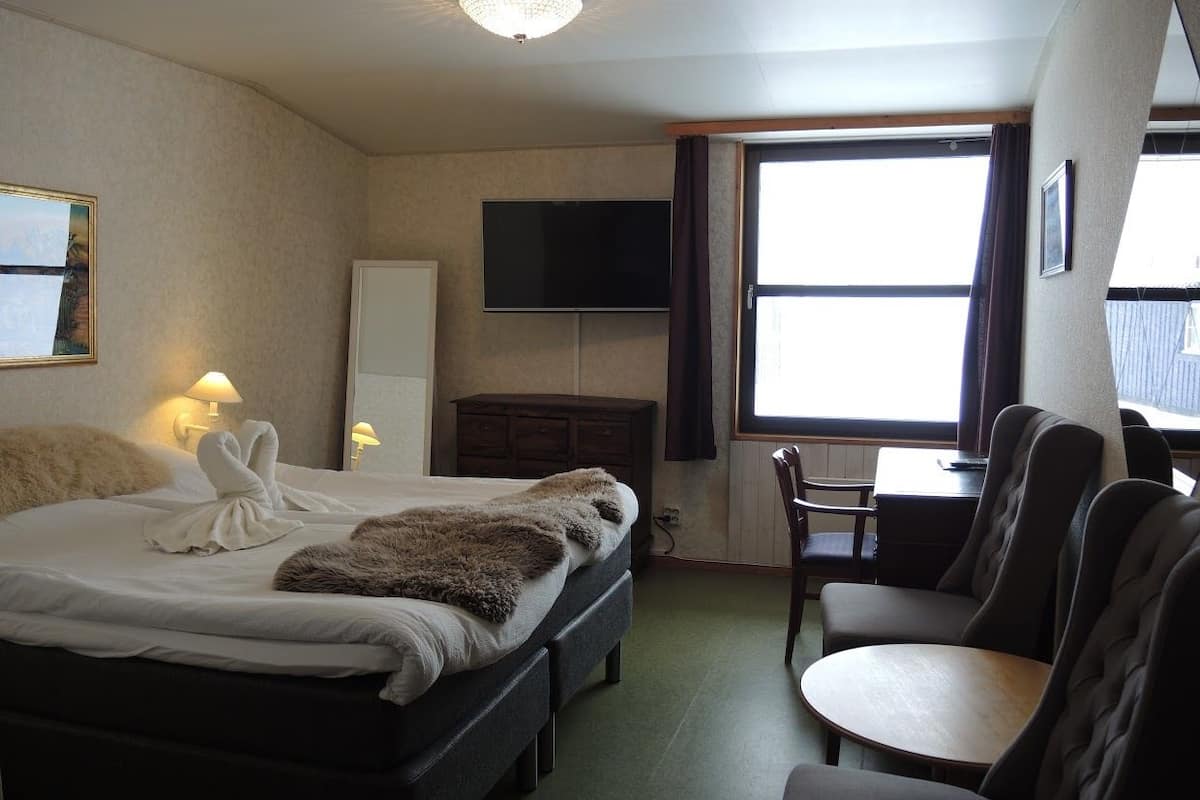 Une chambre d’hôtel avec un lit, un bureau, une chaise, une télévision et une fenêtre.