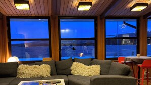 A cozy living room with a sectional sofa, a coffee table, and large windows offering a view of a snowy landscape.