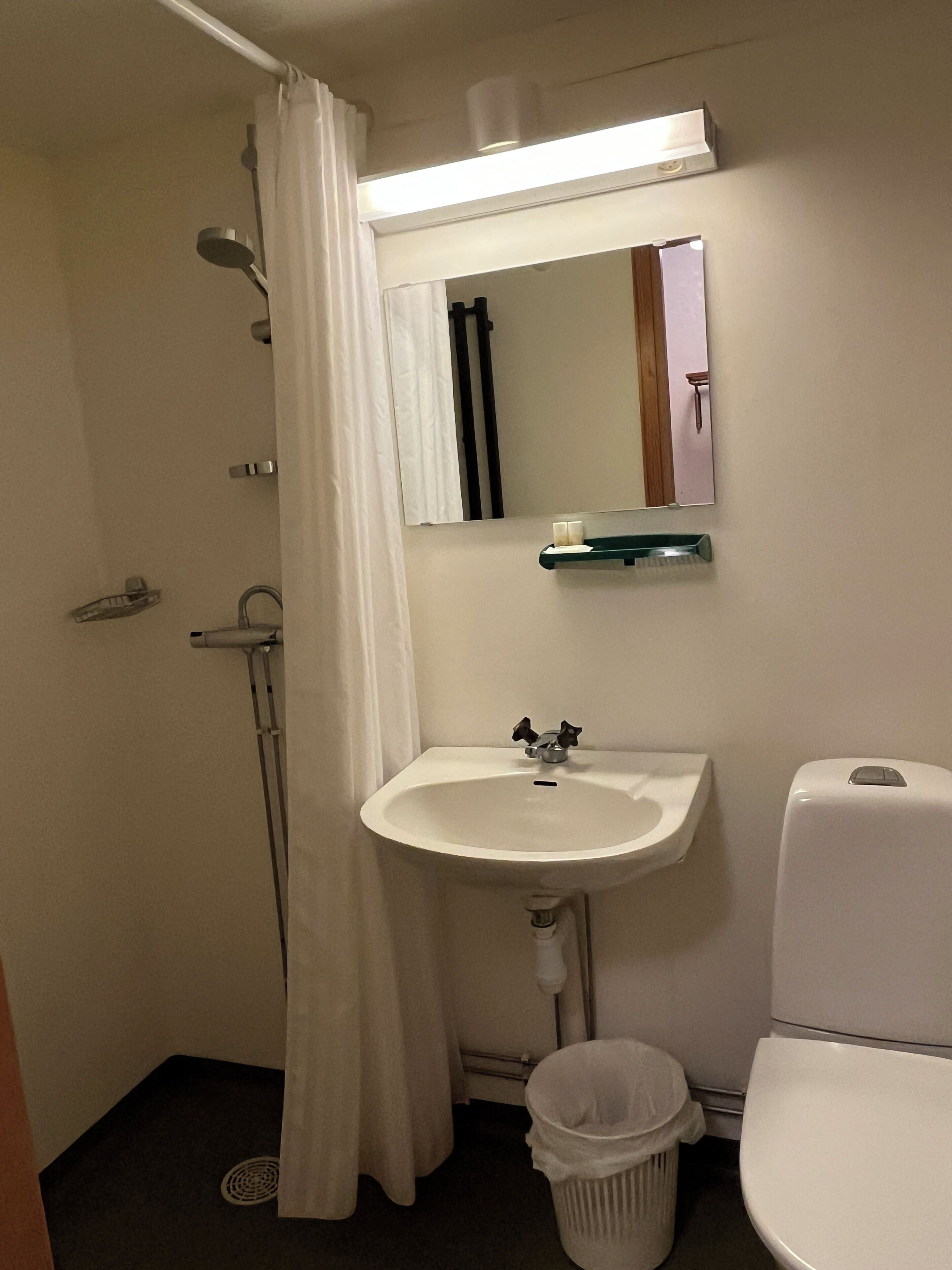 Un baño con un lavamanos blanco, un espejo, un inodoro y una cortina de ducha.