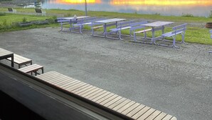 A view of a lakeside picnic area with picnic tables and benches, a grassy area, and a forested hill in the background.