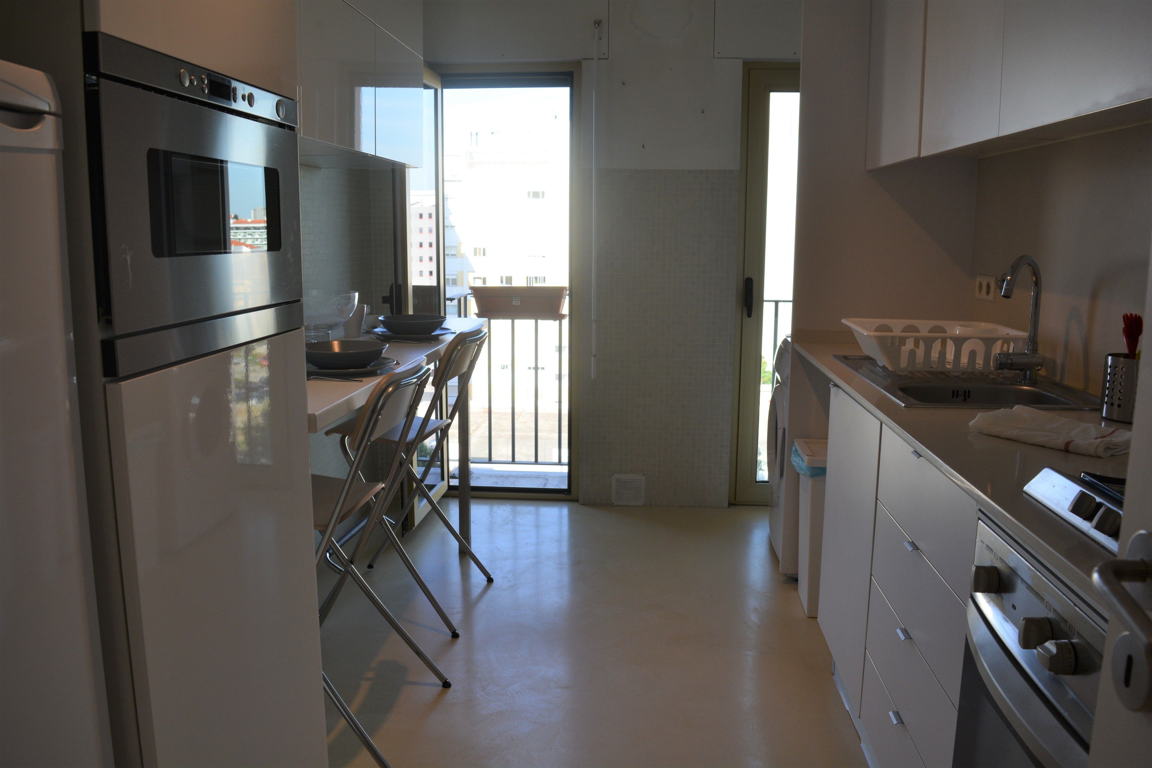 A modern kitchen with stainless steel appliances, a dining area with chairs, and a view through a glass door to the outside.