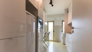 A narrow hallway with a white refrigerator, a small table with chairs, and a door leading to another room. - Modern & Bright by Homing (Lisbon)