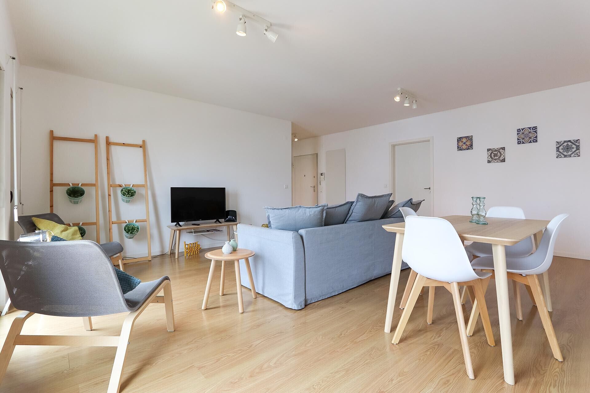 A modern living room with a sofa, a dining table with chairs, a TV, and a wooden floor.