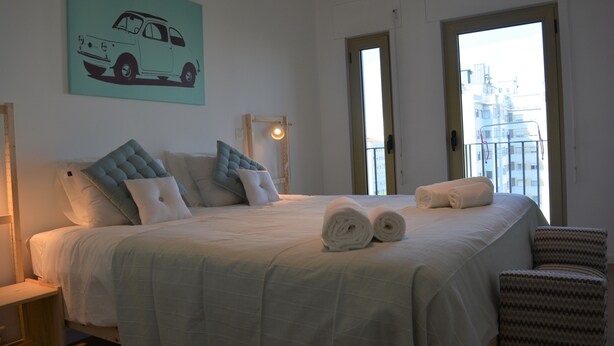 A neatly made bed with pillows, a rolled towel, and a painting of a car on the wall. - Modern & Bright by Homing (Lisbon)