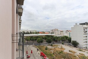 Vista desde un edificio alto sobre un estacionamiento con mesas y sillas rojas, una calle con coches y edificios circundantes.
