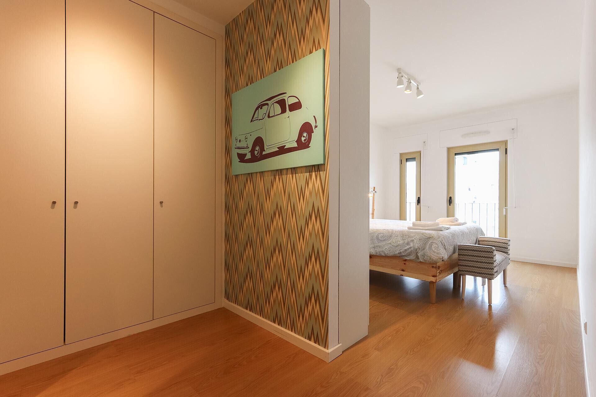 Un dormitorio con una cama, una silla, un armario y una pared con una ilustración de un coche.