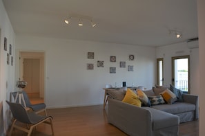 Un salon spacieux avec un canapé gris, une table à manger avec des chaises et un appareil photo fixé sur un trépied.