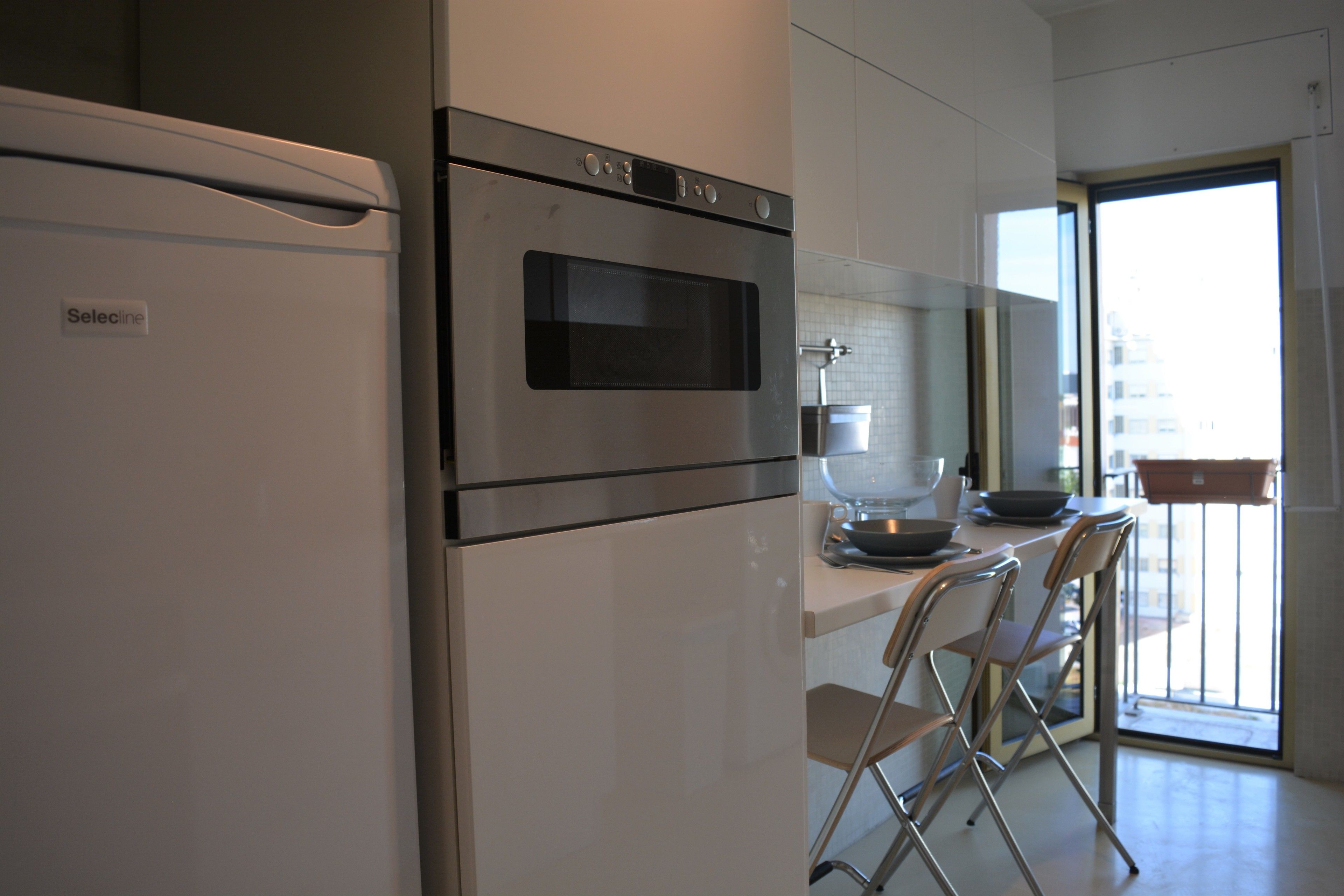 Eine moderne Küche mit Kühlschrank, Backofen und einem Fenster mit Blick auf einen Balkon.