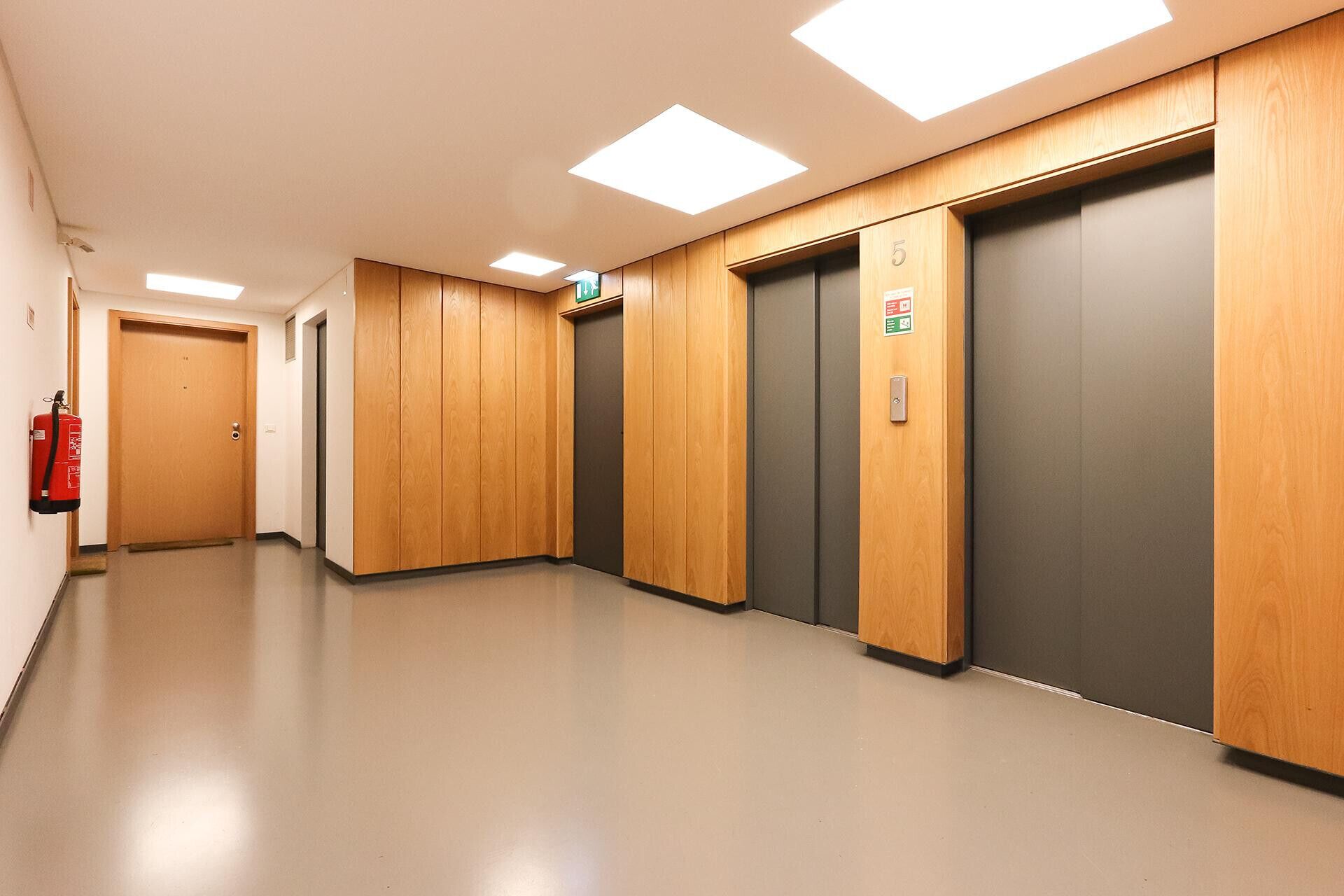 A hallway with wooden paneling, two elevators, and a fire extinguisher on the wall.