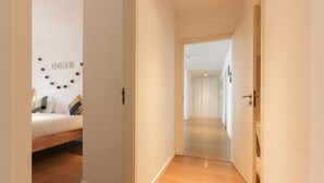 A hallway leading to a bedroom with a bed, a wall decoration spelling "HOME," and a wooden floor. - Modern & Bright by Homing (Lisbon)