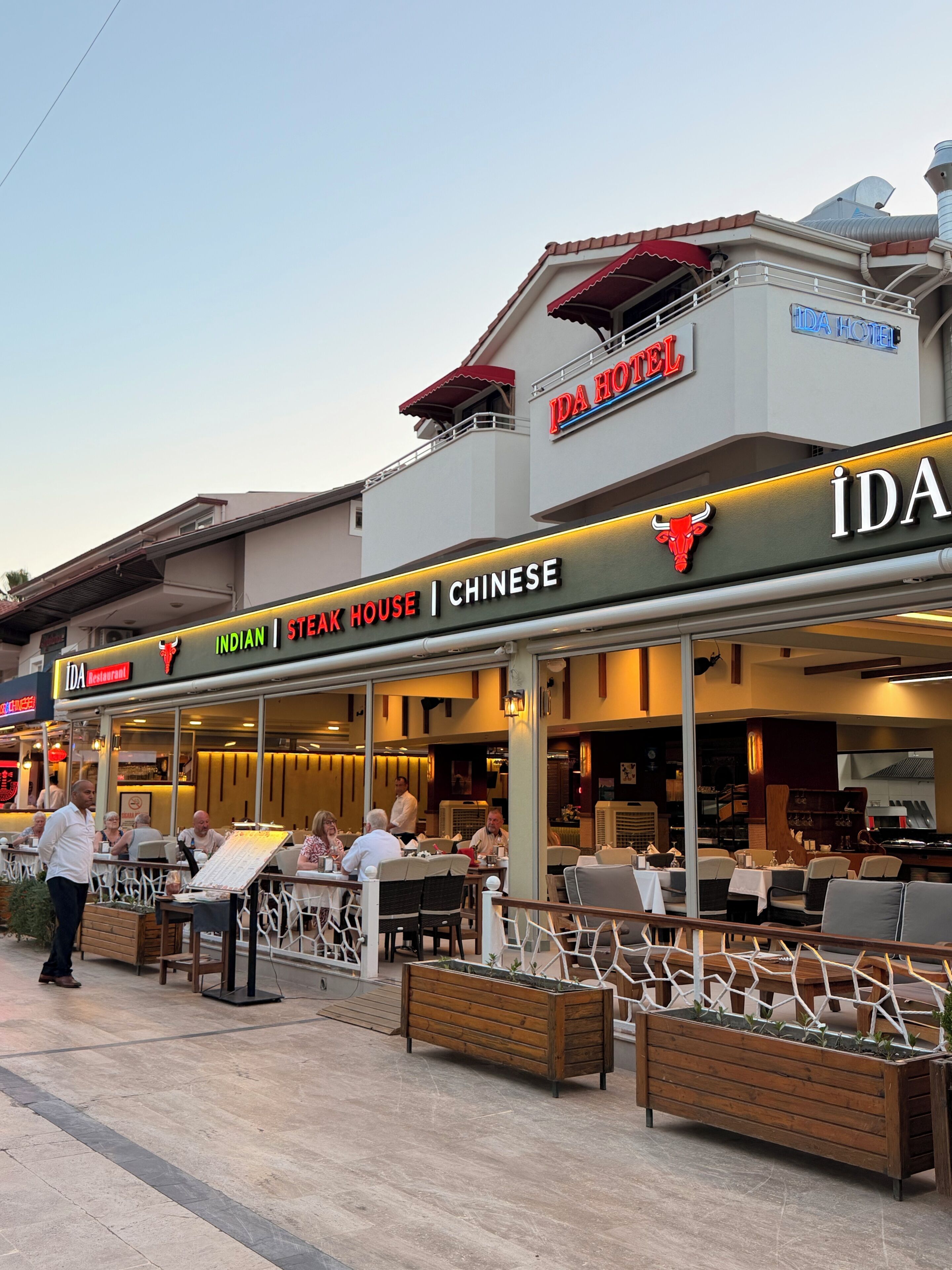A restaurant with outdoor seating, a sign for 'Indian Steak House | Chinese,' and a 'Da Hotel' sign above.