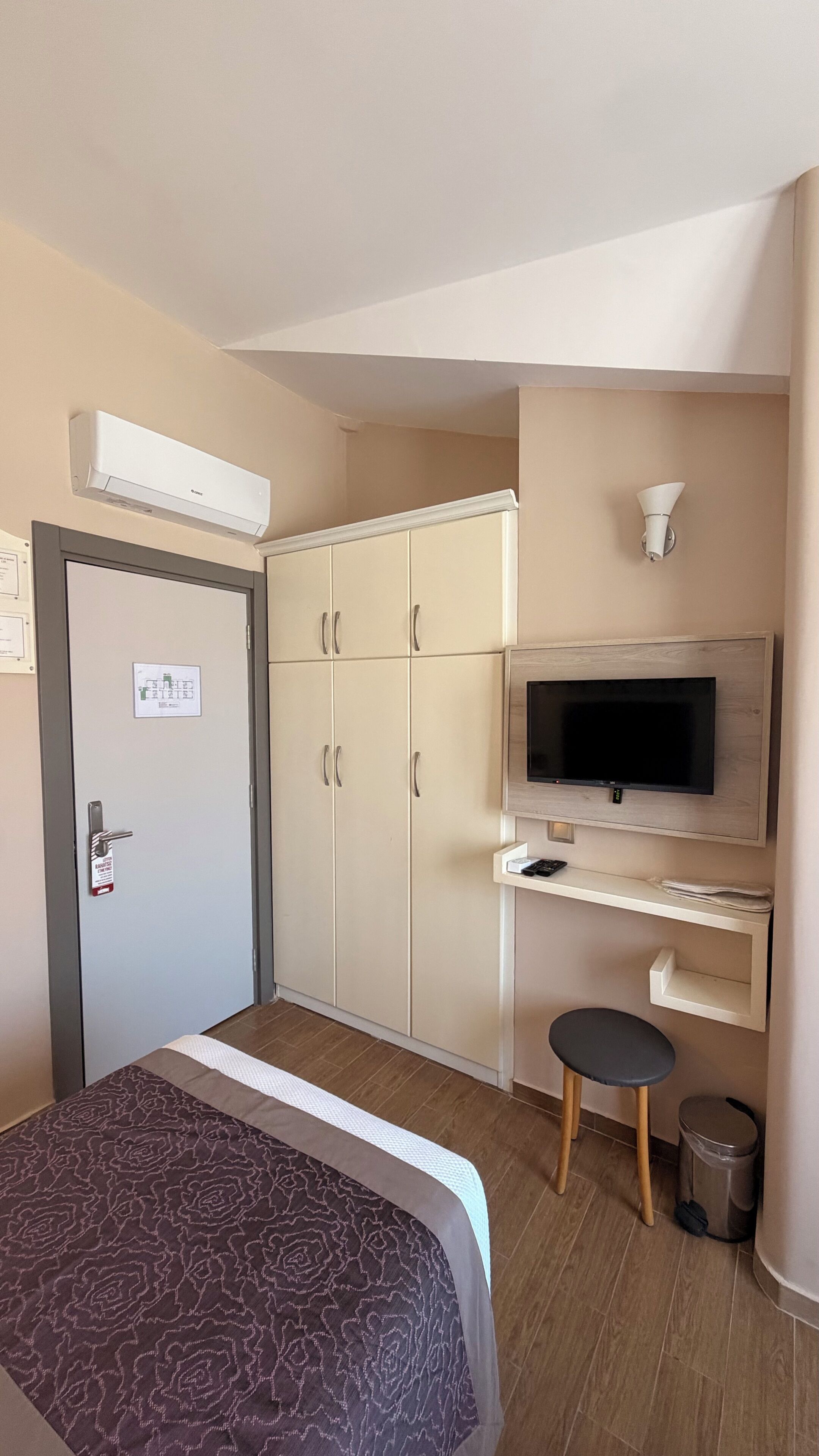 A hotel room with a bed, wardrobe, TV, desk, and a trash bin.