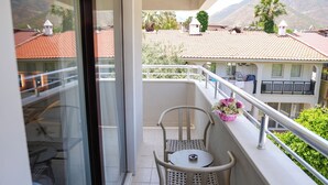 Een balkon met een stoel, een tafel, een glazen deur en uitzicht op gebouwen en bergen.