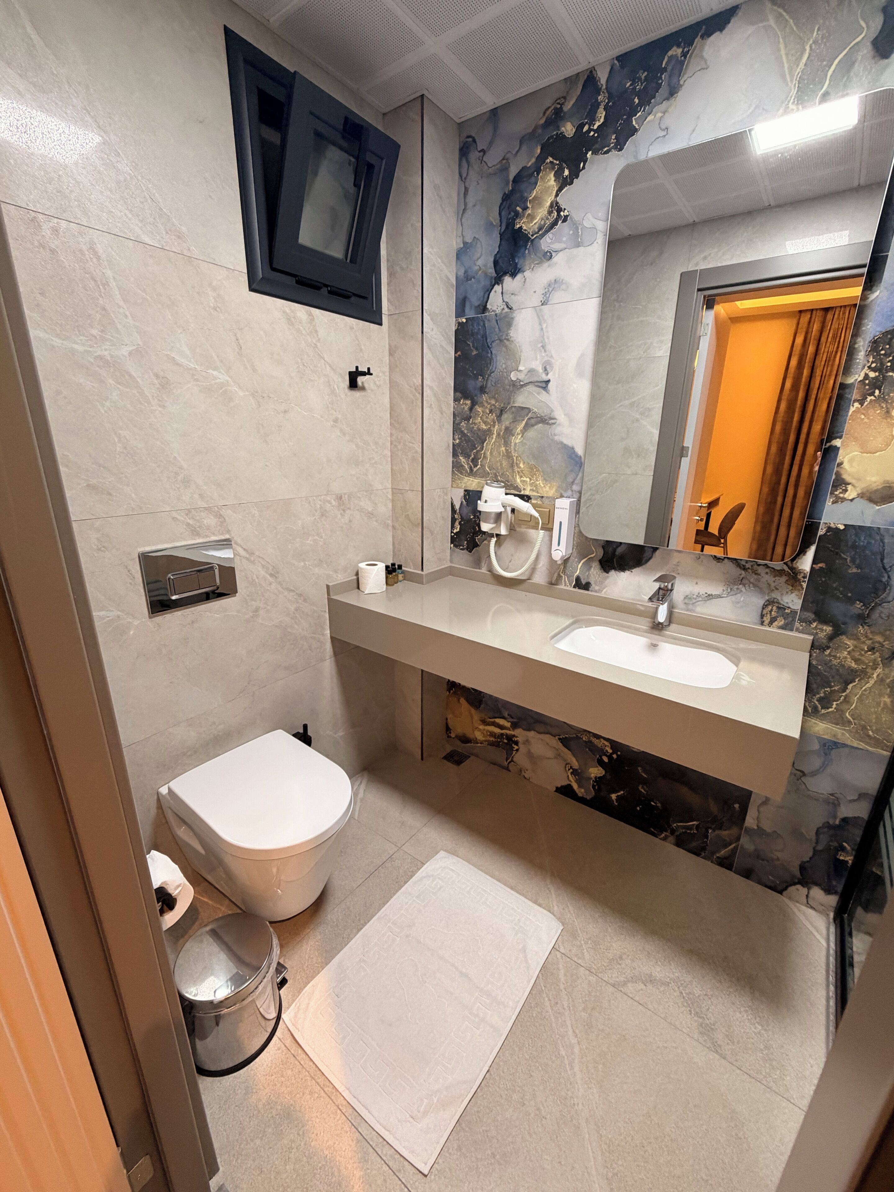 Un baño con inodoro, lavamanos, espejo y pared de mármol.