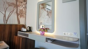 Een badkamer met een houten wastafelmeubel, een spiegel met ingebouwde verlichting, een klein plankje met toiletartikelen en een wandairconditioner.
