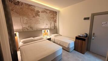 A hotel room with two beds, a large wall mural, bedside lamps, a small table with a kettle, and a door with a sign.
