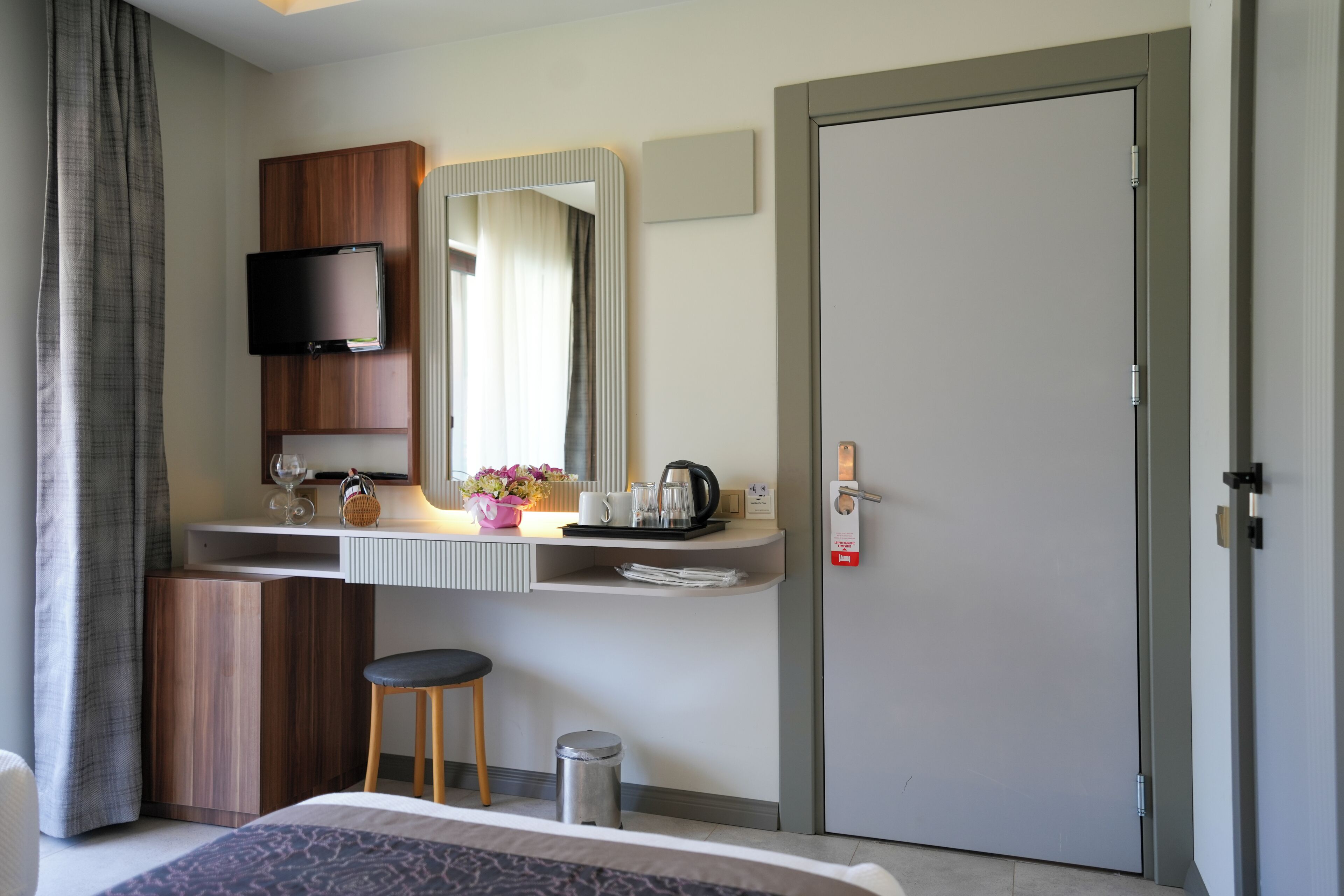A hotel room with a bed, a desk with a mirror, a television, and a door.