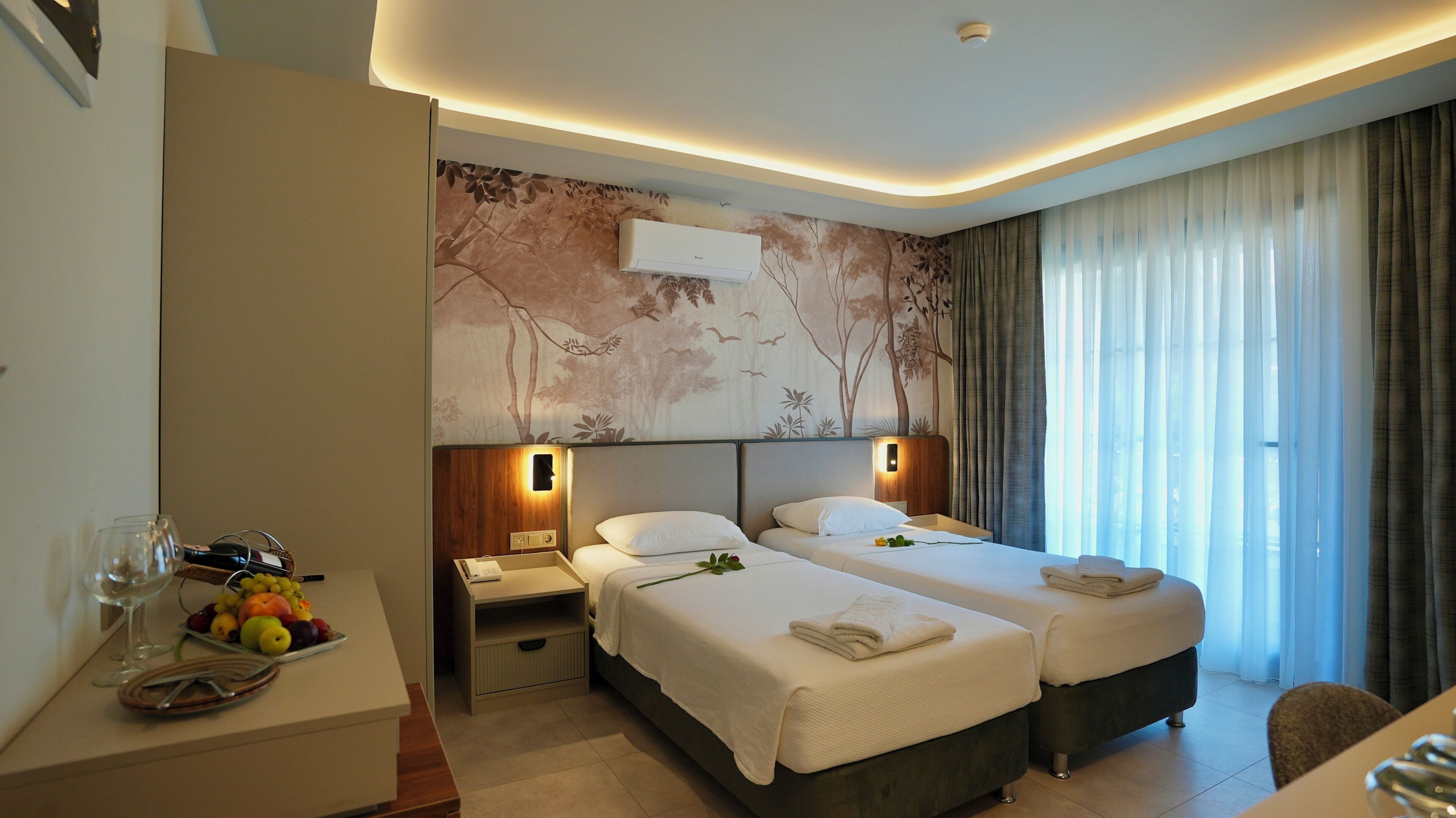 Ein Hotelzimmer mit zwei Betten, einem Schreibtisch mit Obstschale, einem Telefon und einer Wand-Klimaanlage.