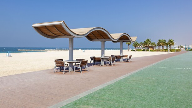 A beachside walkway with outdoor seating and a view of the ocean. - Beach Walk Boutique (Dubai)
