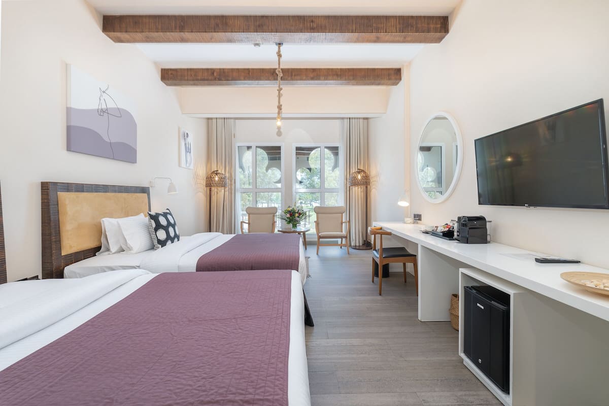 Een hotelkamer met twee bedden, een bureau met een televisie, een spiegel en een raam met gordijnen.