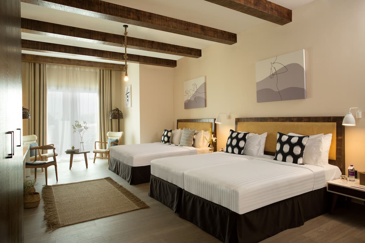 Een hotelkamer met twee bedden, een zithoek met stoelen, een kleine tafel en een groot raam met gordijnen.