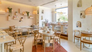 A modern interior with a cozy seating area, a dining space with round tables and chairs, and a large window providing natural light. - Beach Walk Boutique (Dubai)