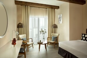 Une chambre d’hôtel avec un lit, deux chaises, une table, une lampe et une fenêtre avec des rideaux.