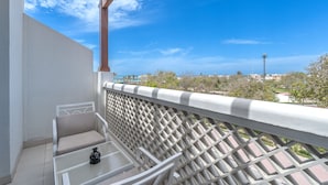 A balcony with a white railing, a cushioned chair, and a small table with a vase. - Beach Walk Boutique (Dubai)