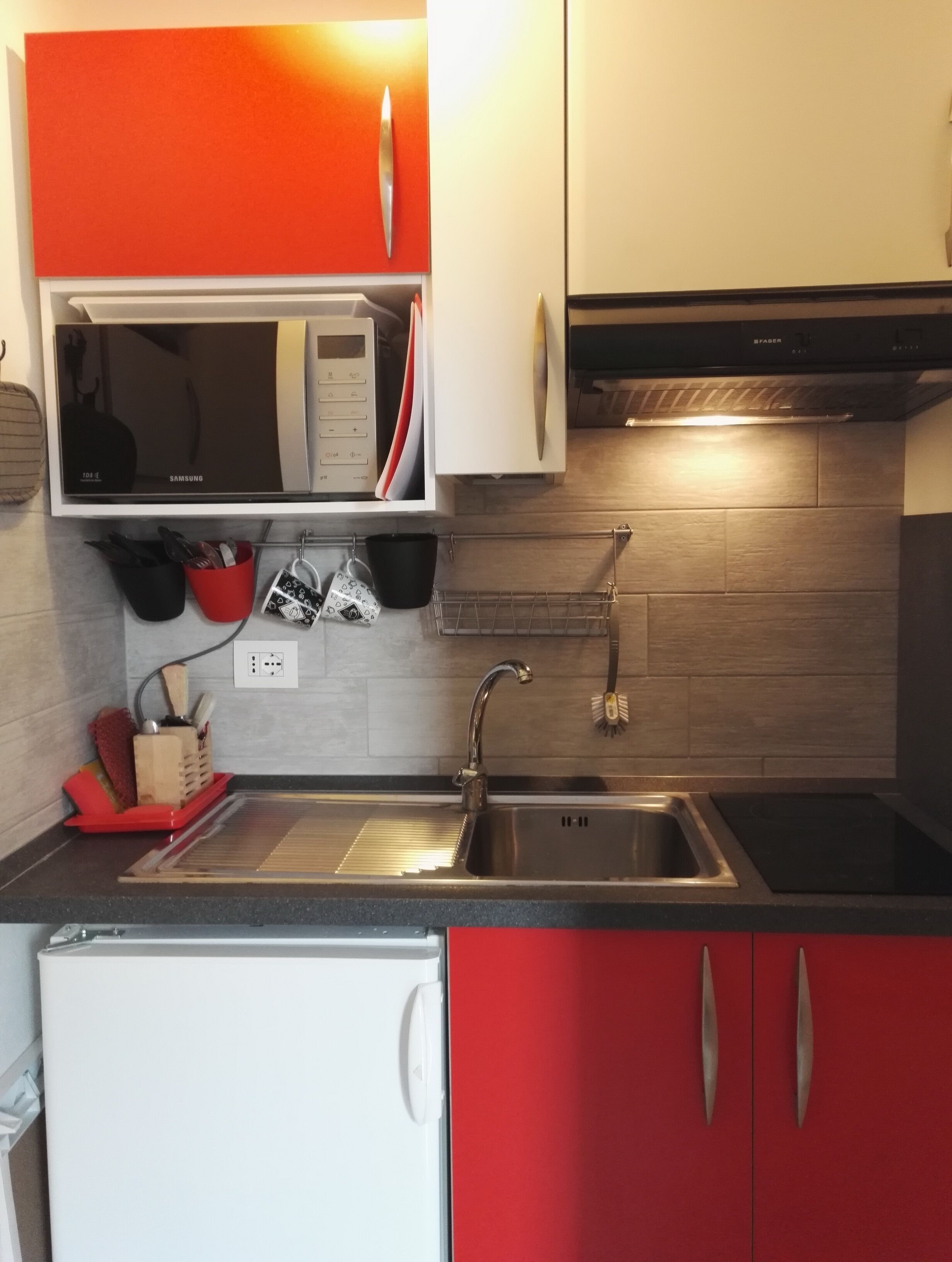 Een keuken met een roestvrijstalen spoelbak, een magnetron en rode kastjes.
