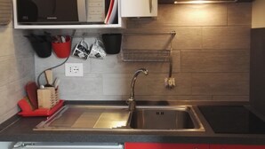 Une cuisine équipée d’un évier en acier inoxydable, d’un four à micro-ondes et de meubles de rangement rouges.