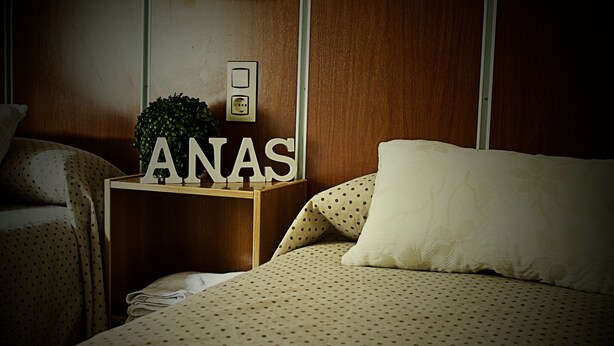 A bedroom with a bed, a nightstand, and a wall-mounted light switch. - Hostal Anas (Merida)