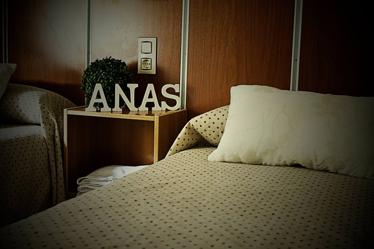 A bedroom with a bed, a nightstand, and a wall-mounted light switch.