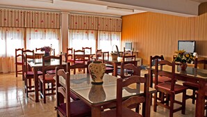 A dining area with wooden chairs and a glass table, featuring a vase with flowers. - Hostal Anas (Merida)