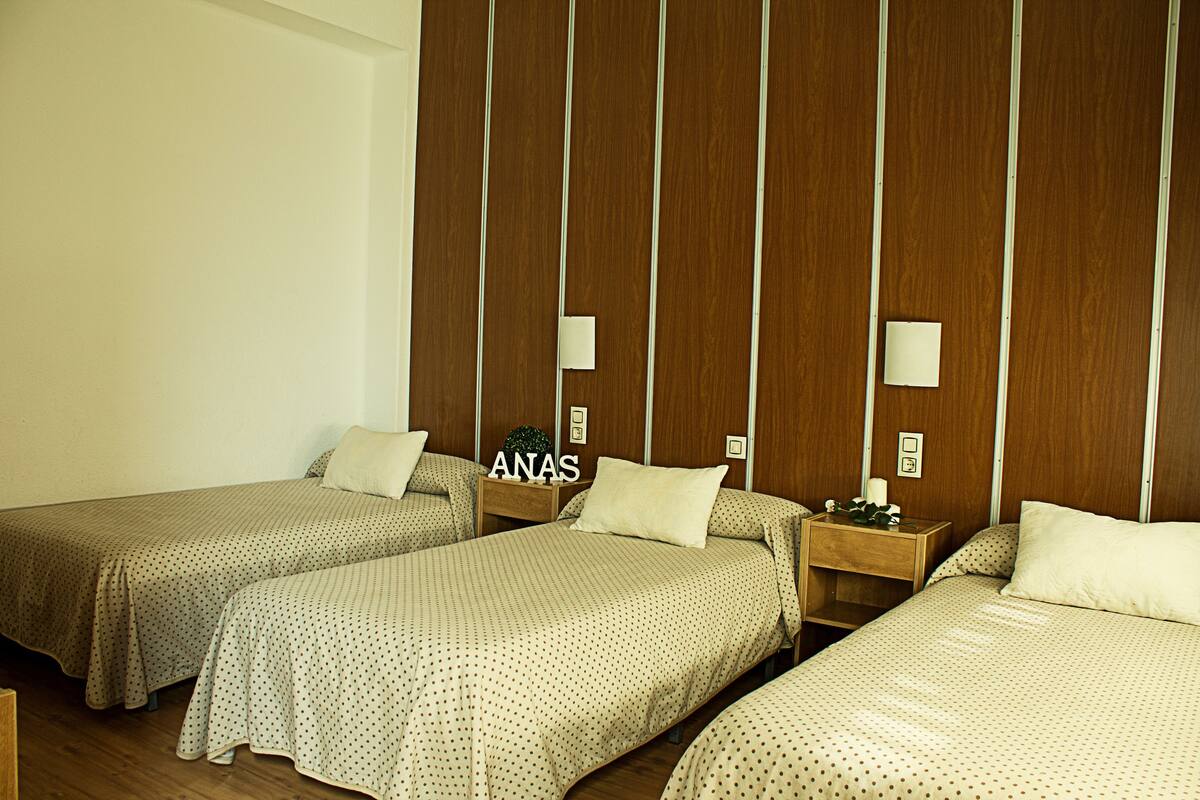 A hotel room with three beds, wooden headboards, and bedside tables with lamps.