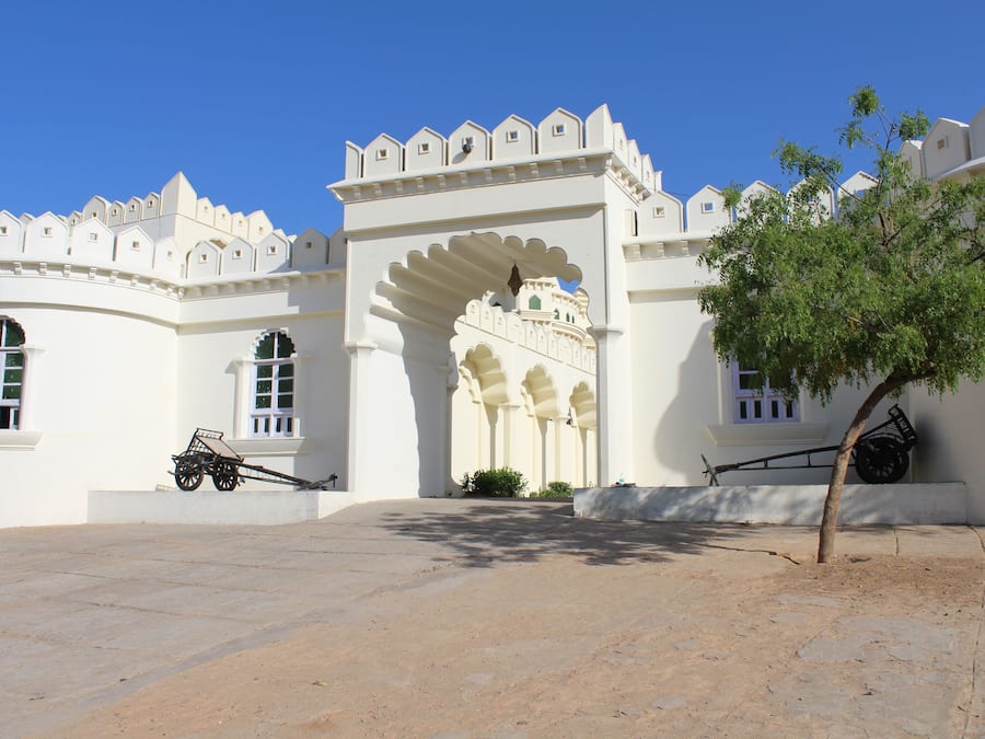 A white building with a large archway and a tree in the foreground.