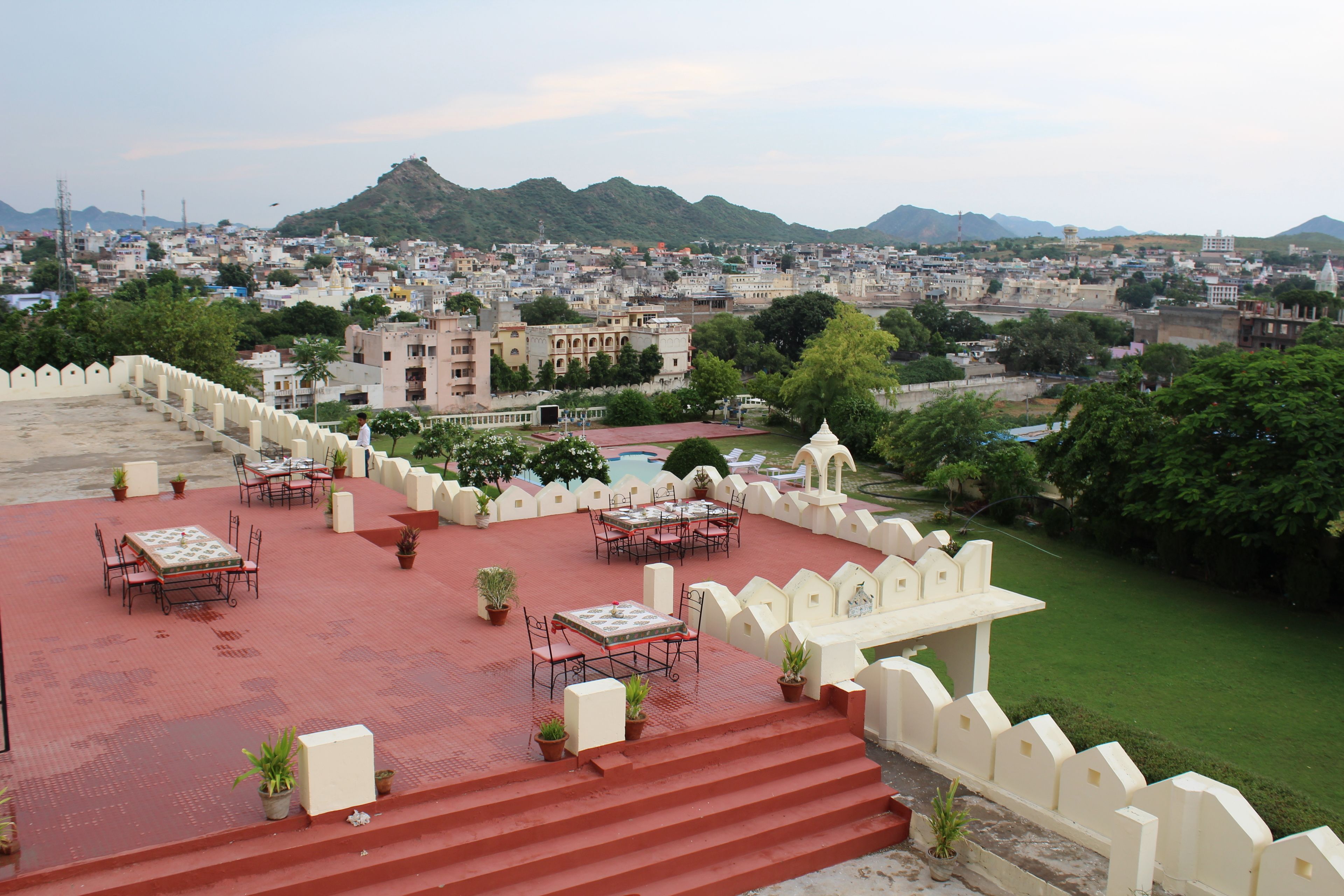 A rooftop terrace with outdoor seating, a pool, and a view of a cityscape with mountains in the background.