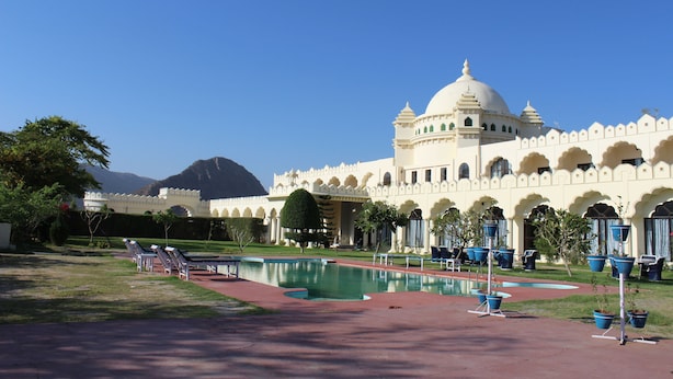 A large, white building with a dome and arched windows, a swimming pool, and lounge chairs in the foreground. - Gulaab Niwaas Palace (Pushkar)