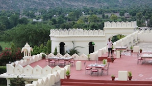 A rooftop restaurant with outdoor seating, white architectural design, and a view of a green landscape. - Gulaab Niwaas Palace (Pushkar)