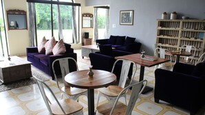 A living room with a purple sofa, white chairs, a wooden coffee table, and a bookshelf. - Gulaab Niwaas Palace (Pushkar)