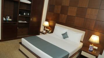A hotel room with a bed, a nightstand with a lamp, a wardrobe, and a desk with a telephone.