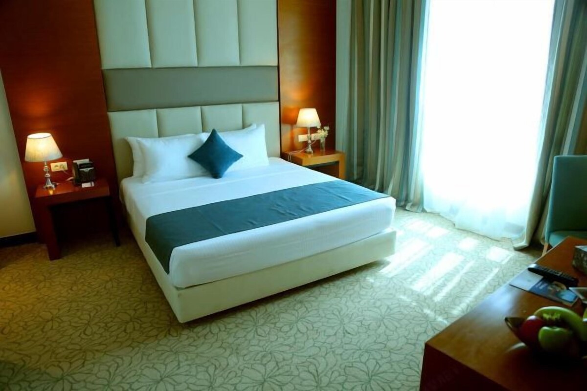 Habitación de hotel con una cama grande, dos mesitas de noche con lámparas, un televisor de pantalla plana y un frutero en la mesita auxiliar.