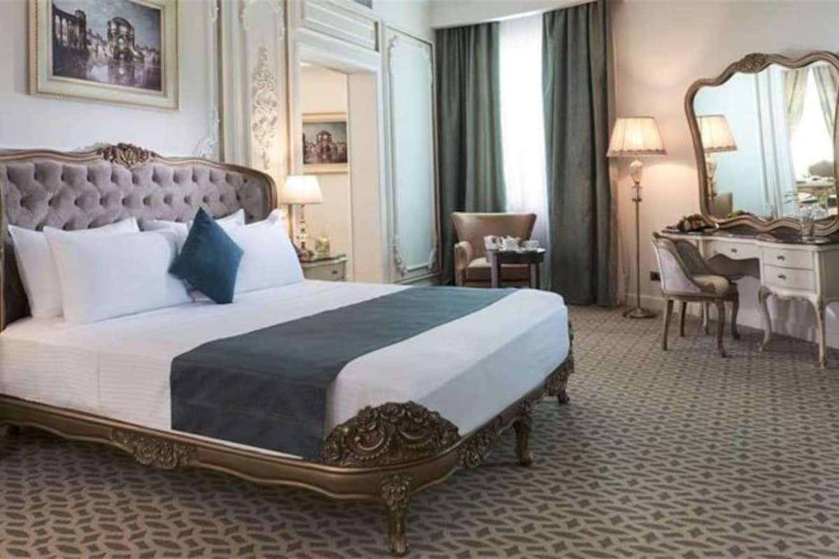 A hotel room with a large bed, a desk, a chair, and a mirror.